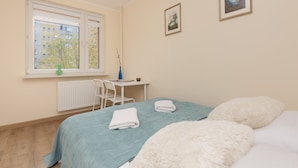 Un dormitorio con cama, escritorio, silla y ventana con vista a edificios.