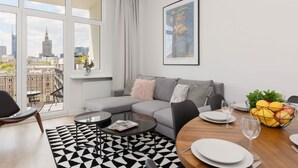 A modern living room with a grey sofa, a round dining table set for two, a black and white rug, and a large window with a city view. - Stylish Apartment in the Center | Air Conditioning (Warszawa)