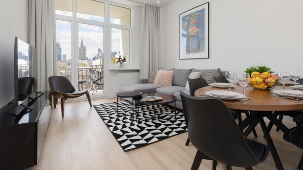 A modern living room with a sofa, dining table, chairs, a coffee table, and a city view through large windows. - Stylish Apartment in the Center | Air Conditioning (Warszawa)