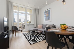 A modern living room with a sofa, dining table, chairs, a coffee table, and a city view through large windows. - Stylish Apartment in the Center | Air Conditioning (Warszawa)