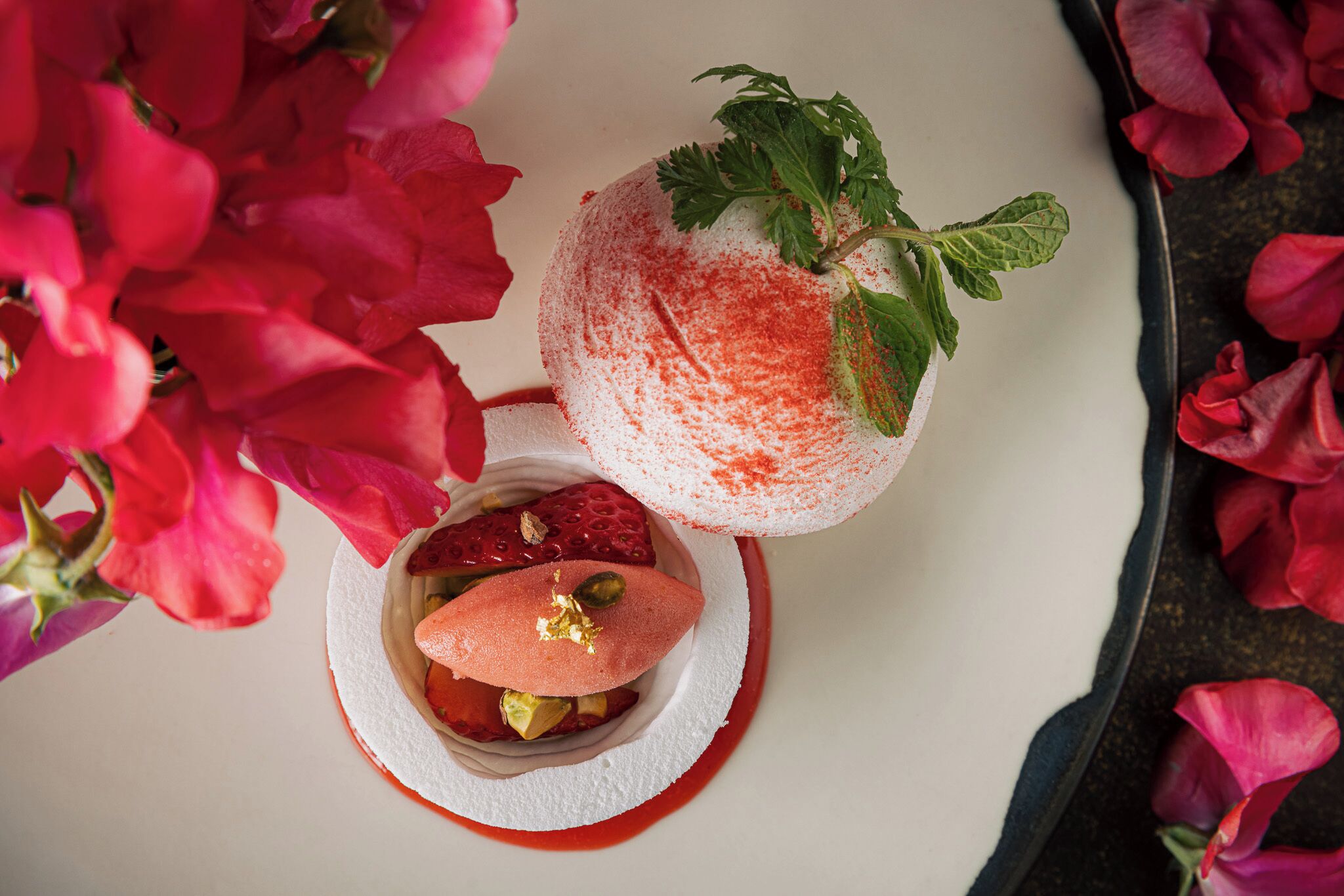Dessert met aardbeien en muntblaadjes op een wit bord.
