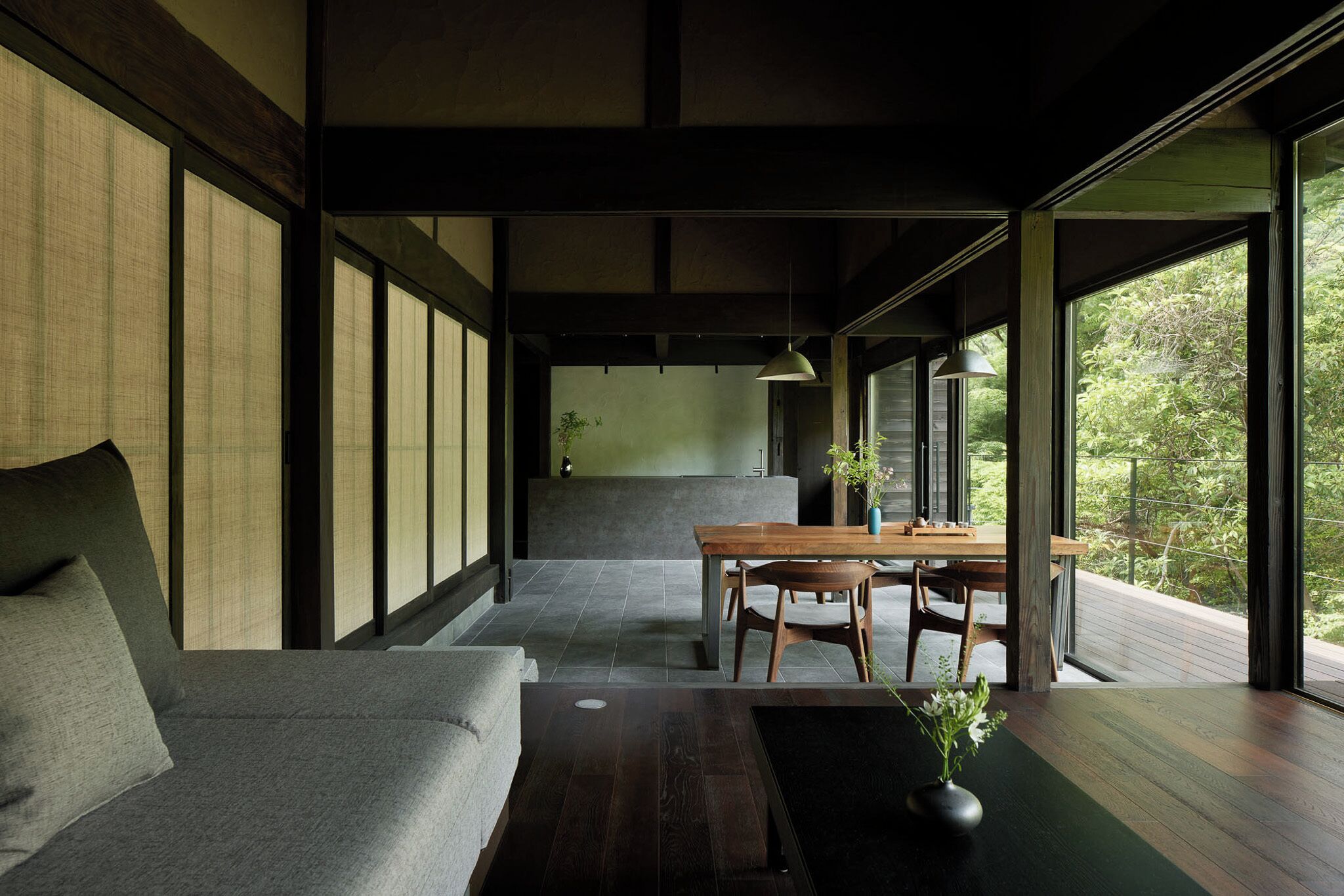 Un intérieur moderne avec un canapé, une table à manger et des chaises, ainsi que de grandes fenêtres donnant sur un paysage verdoyant.