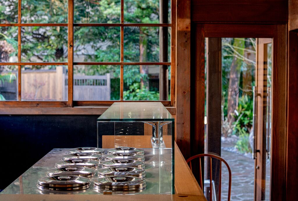 Una cocina con una mesa de vidrio, una estufa de metal y vistas al verdor a través de una ventana.