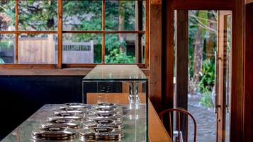 Una cocina con una mesa de vidrio, una estufa de metal y vistas al verdor a través de una ventana.