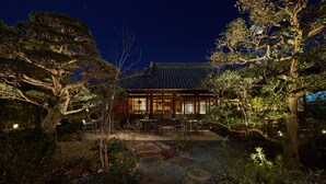 A traditional Japanese house with a tiled roof, surrounded by large trees and a stone pathway leading to the entrance. - Loquat Nishiizu (Izu)