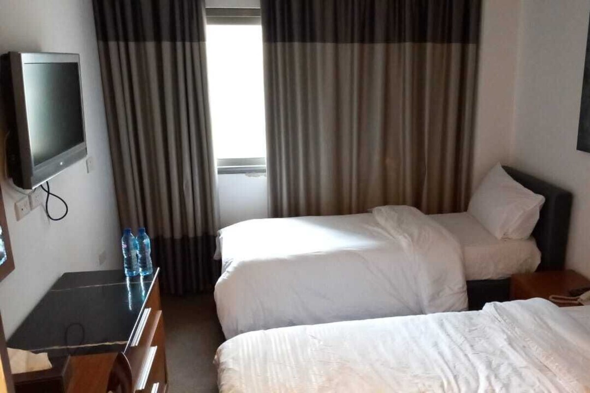 A hotel room with two beds, a TV, a desk, and a window with curtains.