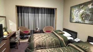 A hotel room with two beds, a desk with a computer, a chair, a small table with a lamp, and a painting on the wall. - City Suite Hotel (Beirut)