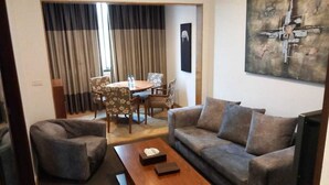 A living room with a sofa, armchair, coffee table, and a dining area with a table and chairs. - City Suite Hotel (Beirut)