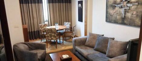 A living room with a sofa, armchair, coffee table, and a dining area with a table and chairs.