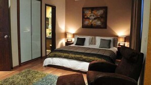 A bedroom with a bed, two bedside tables, a chair, a painting on the wall, and a wardrobe. - City Suite Hotel (Beirut)