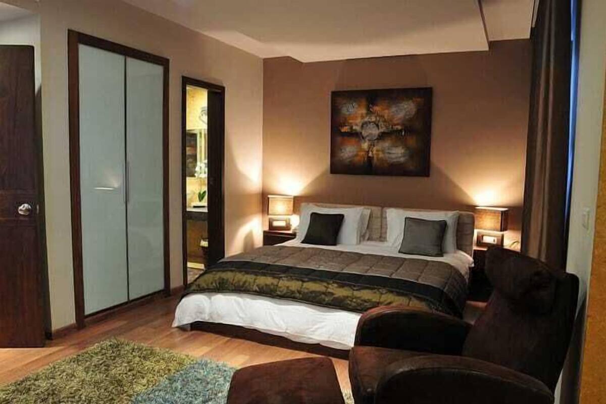 Ein Schlafzimmer mit einem Bett, zwei Nachttischen, einem Sessel, einem Bild an der Wand und einem Kleiderschrank.