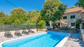 A rectangular swimming pool with a tiled edge, surrounded by a stone patio. There are four lounge chairs aligned along the poolside. A stone building with a tiled roof and green shutters is visible in the background. - Lovely home in Donji Vinjani (Donji Vinjani)