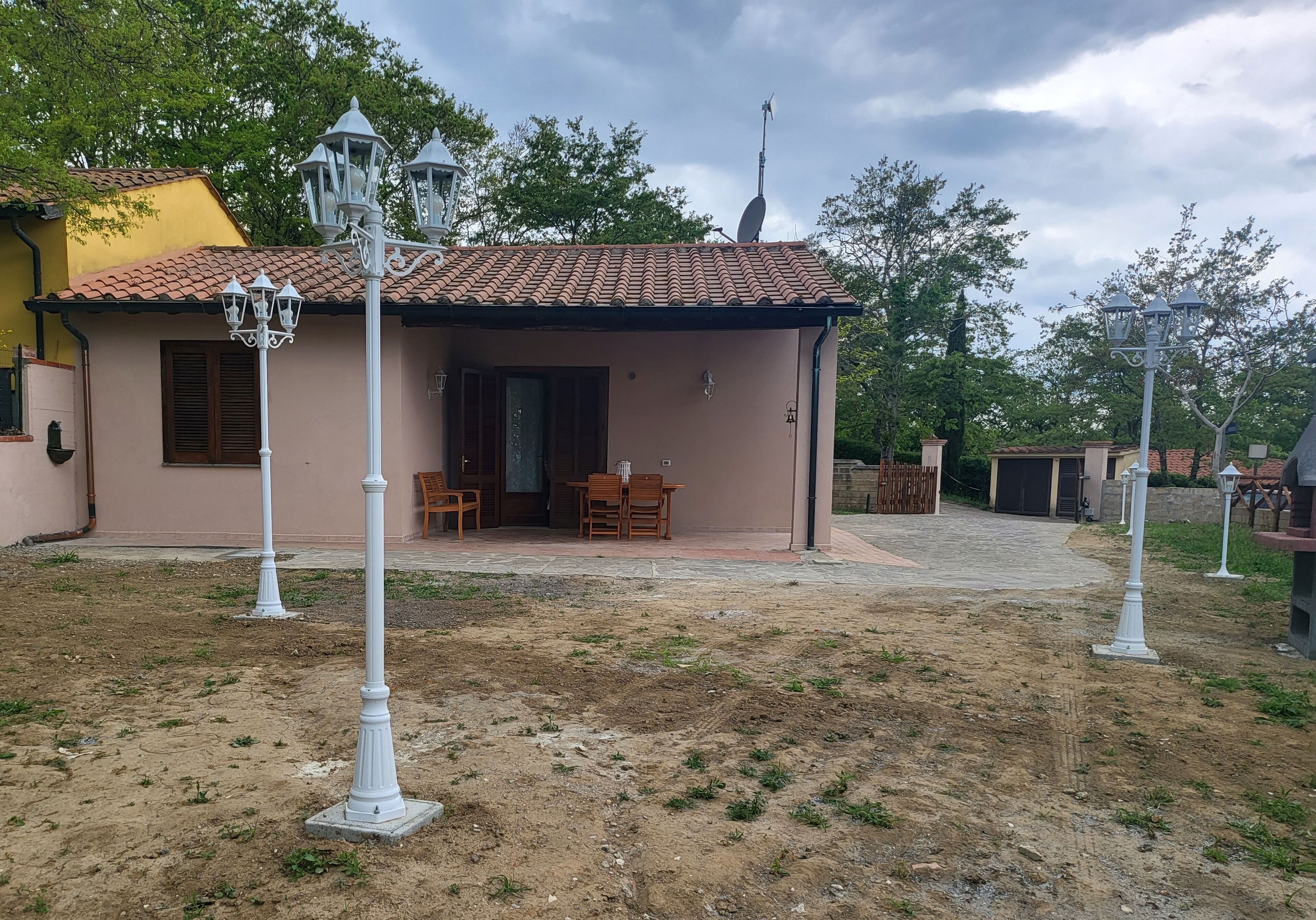 A single-story house with a tiled roof, a porch with wooden furniture, and a satellite dish.