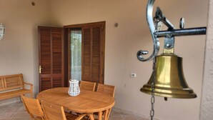 Una mesa de madera con sillas, un farol blanco y una campana colgada de una cadena.