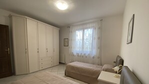 Un dormitorio con dos camas, un armario, una mesita de noche con lámpara y una ventana con cortinas.
