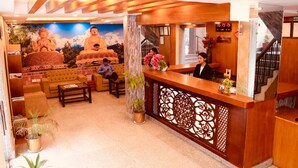 A reception area with a wooden reception desk, a sofa, a coffee table, and a mural of Buddha statues. - Satkar Hotel and Spa (Kathmandu)