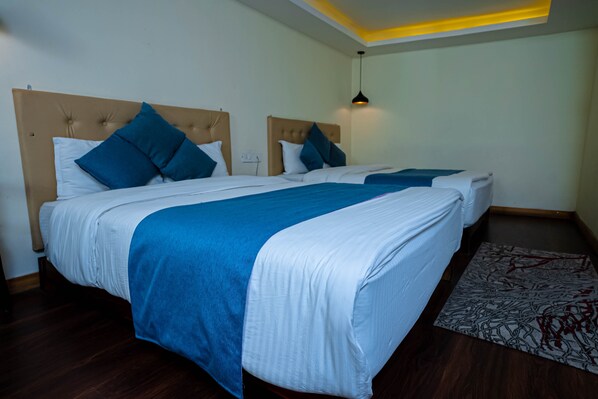 Habitación de hotel con dos camas, cada una con cabecero, una manta azul y una colcha blanca. Hay una alfombra pequeña con un estampado rojo y negro en el suelo.