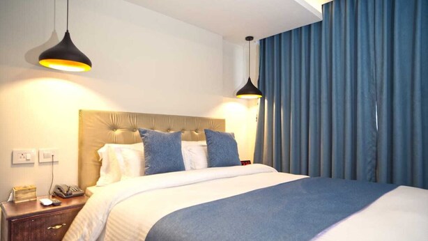 A hotel room with a large bed, two bedside lamps, a wooden nightstand, a telephone, and a blue curtain. - Satkar Hotel and Spa (Kathmandu)
