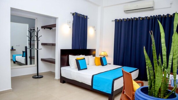 A hotel room with a bed, a chair, a potted plant, and a coat rack. - HOTEL ACRUS (Galle)
