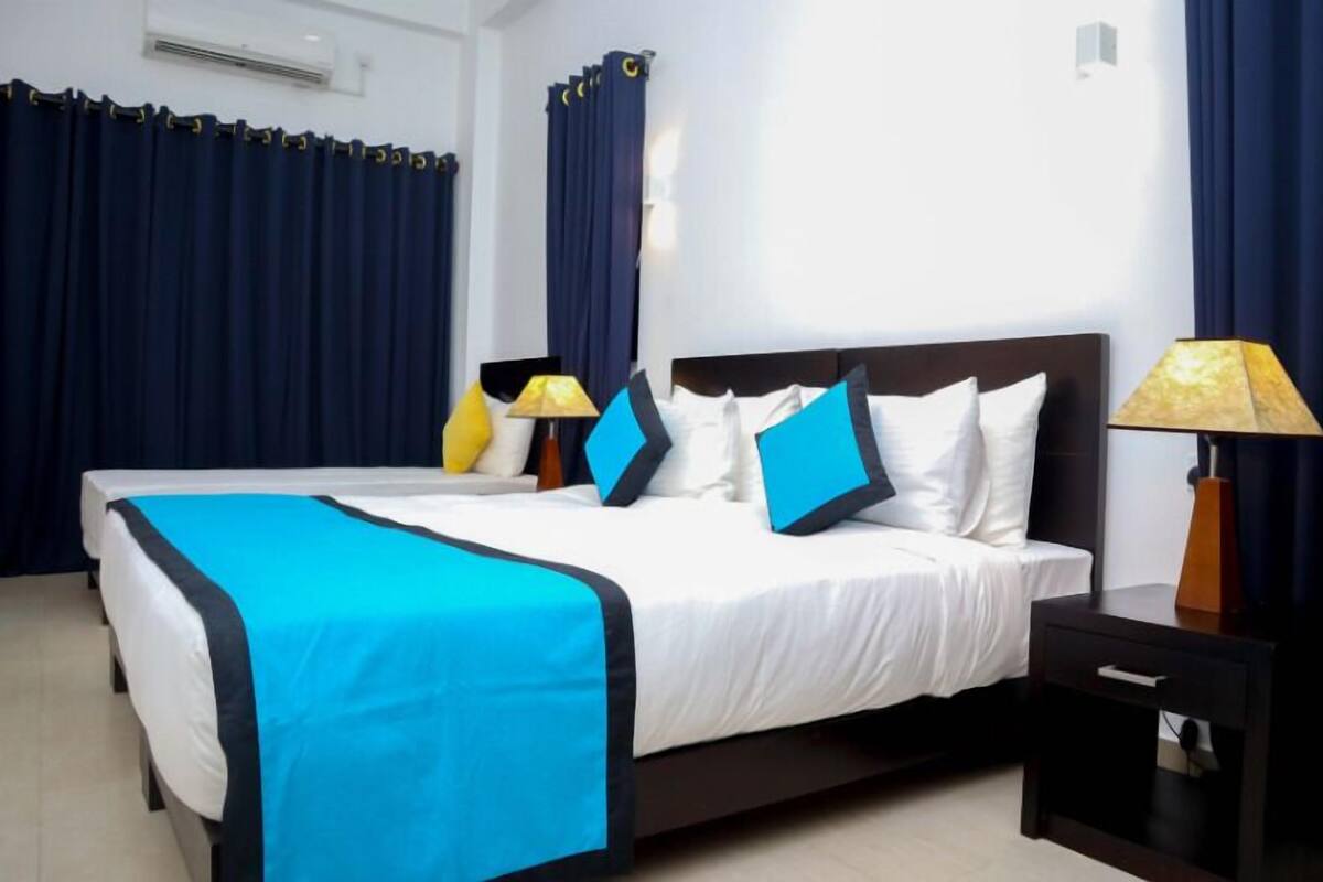 A hotel room with a large bed, dark curtains, a bedside lamp, and a small table.