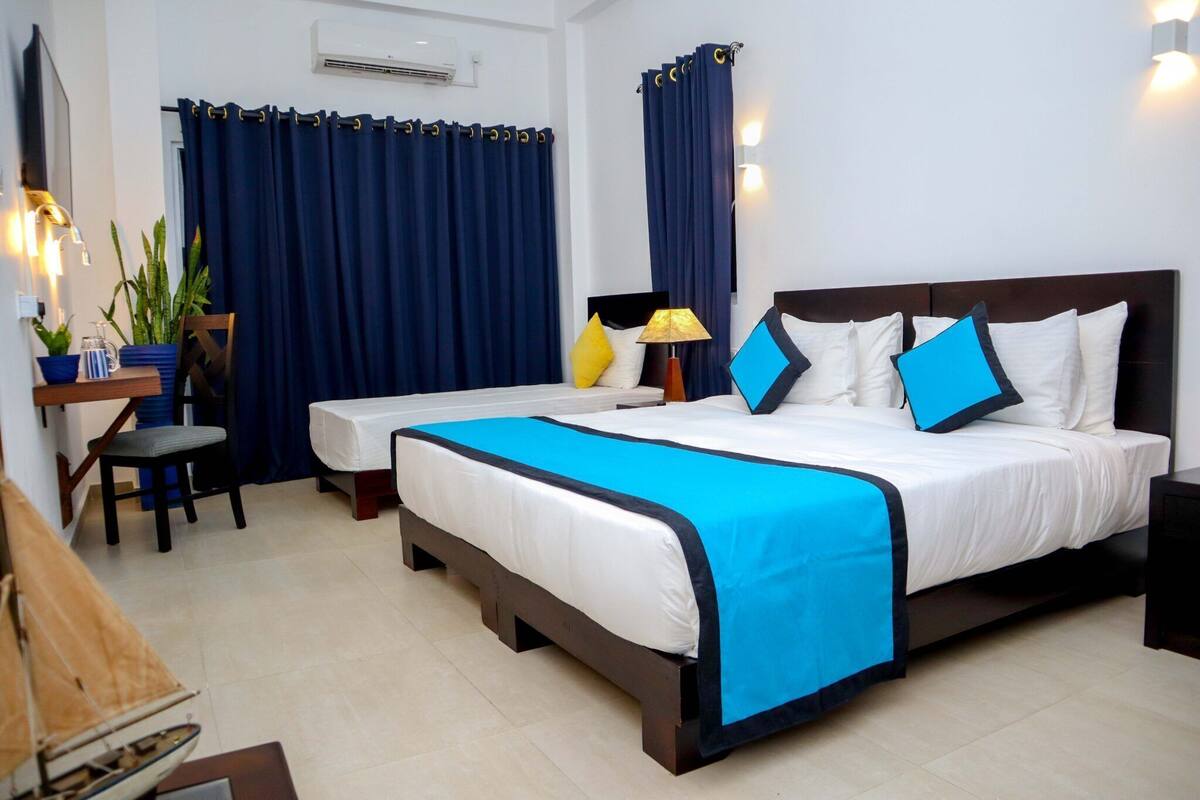 A hotel room with a large bed, a desk with a chair, a lamp, and curtains.