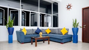 A modern living room with a blue sofa, yellow and blue cushions, a glass coffee table, and two blue planters. - HOTEL ACRUS (Galle)