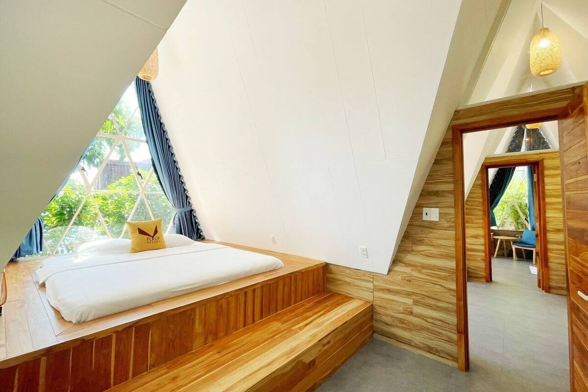 A bedroom with a wooden bench, a bed with a pillow, and a view of greenery outside.