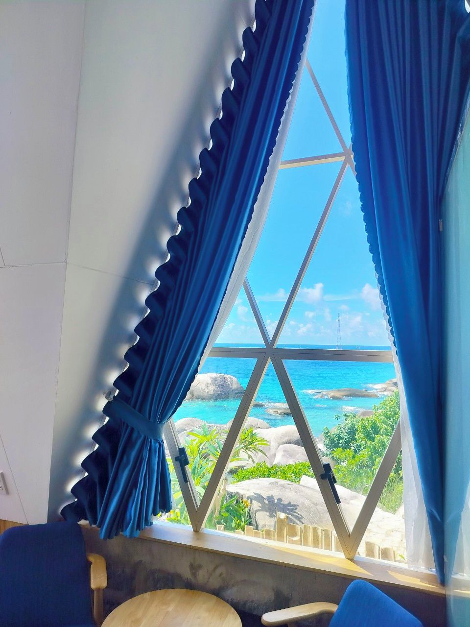 Una habitación con vistas al océano a través de una ventana con cortinas azules.