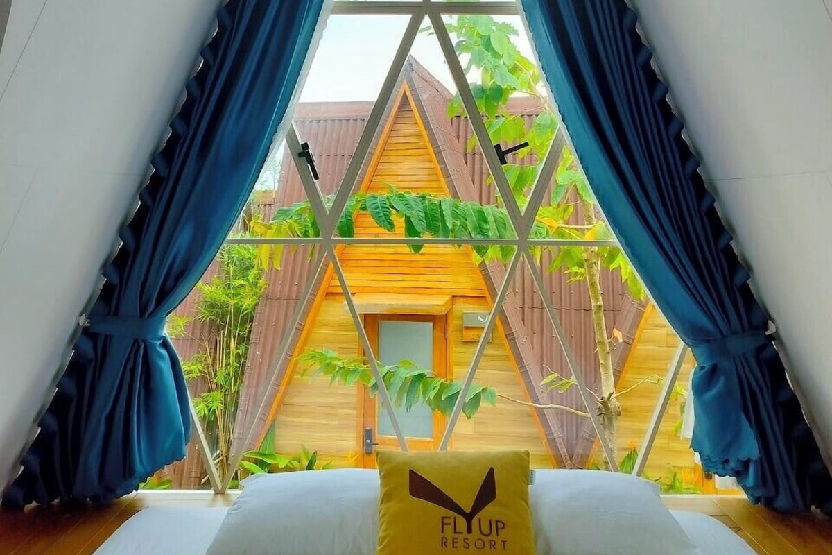 A bed with a pillow labeled "FLIP RESORT" in a room with a view of a wooden structure and greenery outside.
