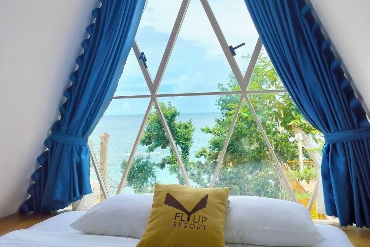 A bedroom with a bed, a pillow with a logo, and a window with curtains.