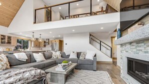 Una sala de estar moderna con un sofá seccional gris, una chimenea y una escalera que sube a un nivel superior.
