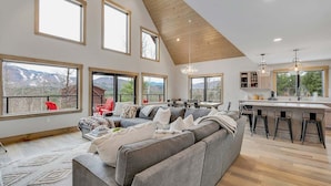 Amplia sala de estar con techo alto, ventanas grandes, cocina moderna y una zona de estar acogedora.