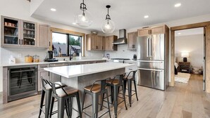 Una cocina moderna con una isla grande, taburetes de bar, electrodomésticos de acero inoxidable y armarios de madera.