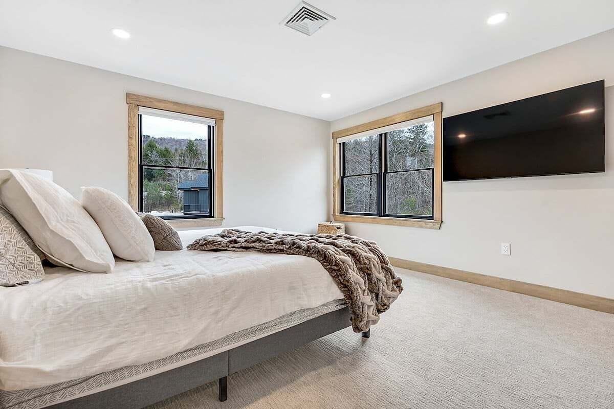 Een slaapkamer met een bed, twee ramen, een flatscreen-tv en een ventilatie rooster.