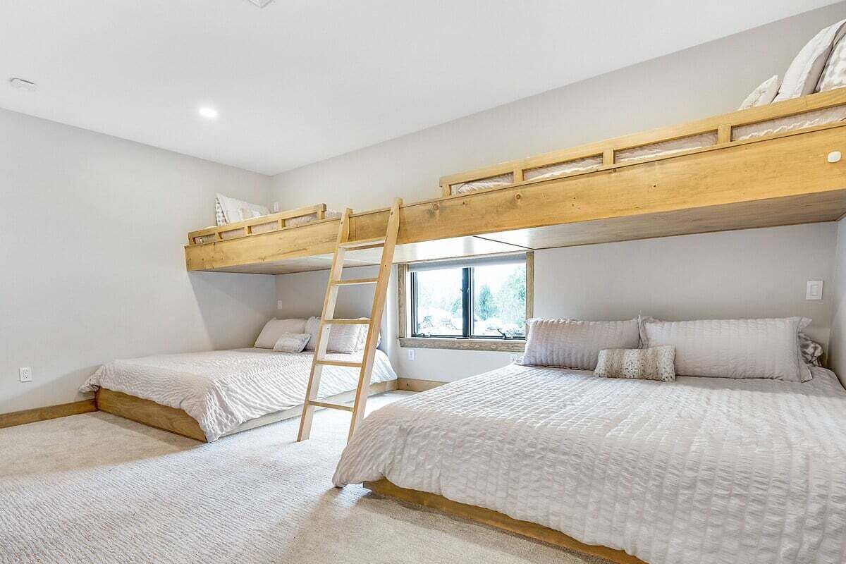A bunk bed room with a ladder, a window, and a carpeted floor.