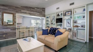 Un salon avec un canapé beige, une table basse et une bibliothèque remplie de divers objets.