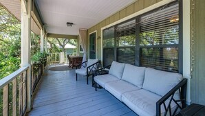 Une véranda avec un canapé et des fauteuils blancs, une table et une vue sur l’extérieur.