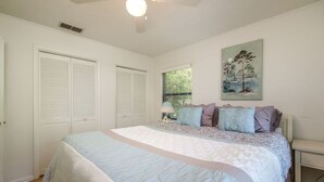 Une chambre à coucher avec un lit, un ventilateur de plafond, une fenêtre avec des stores et un tableau au mur.