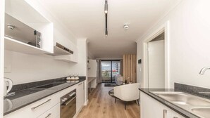 A modern kitchen with white cabinetry, a black countertop, and a wooden floor. - Colourful and Cosy Studio Apartment in Newlands (Cape Town)