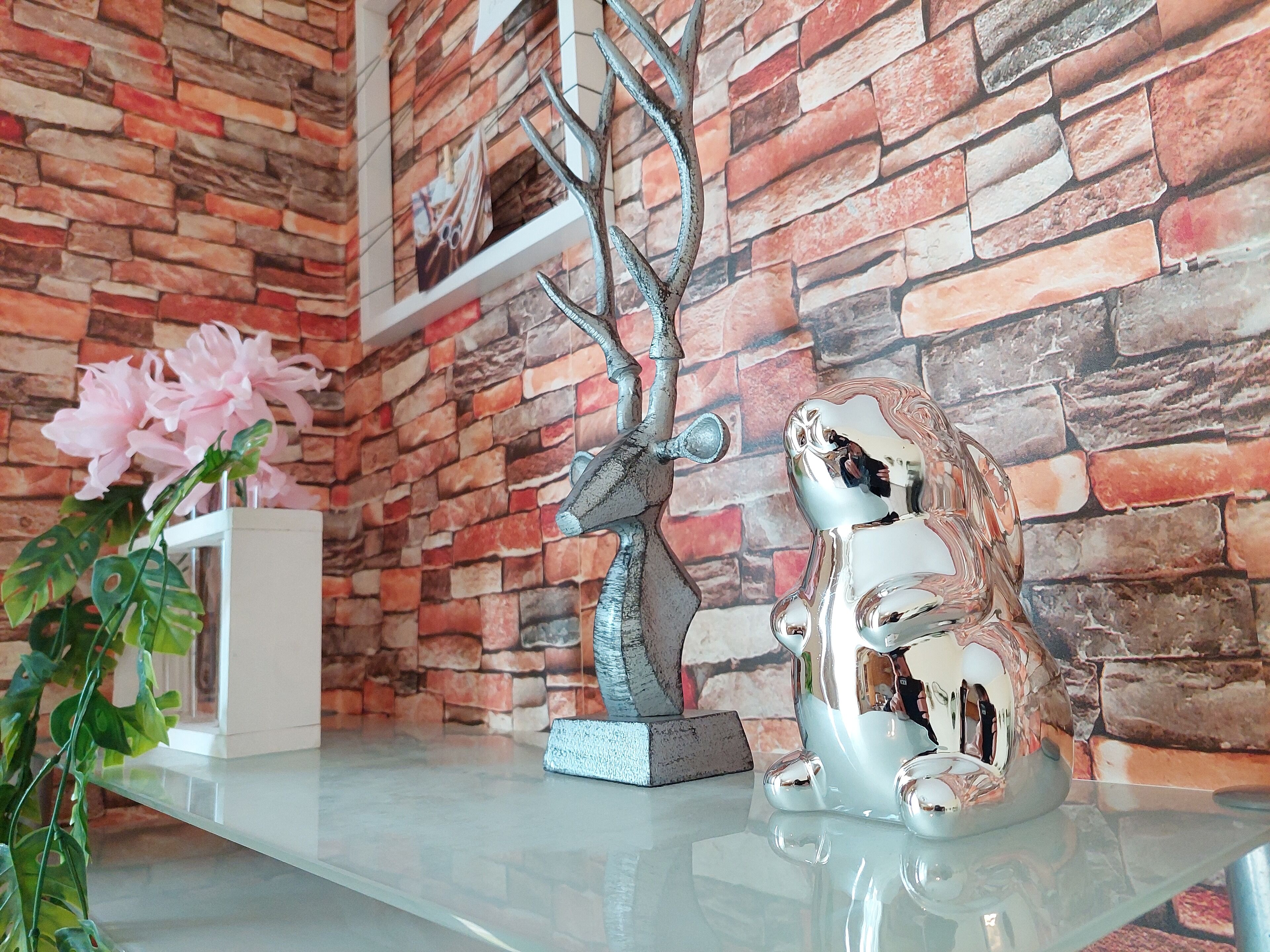 A room with a brick wall, a glass table, and decorative items including a tree sculpture and a ceramic frog.