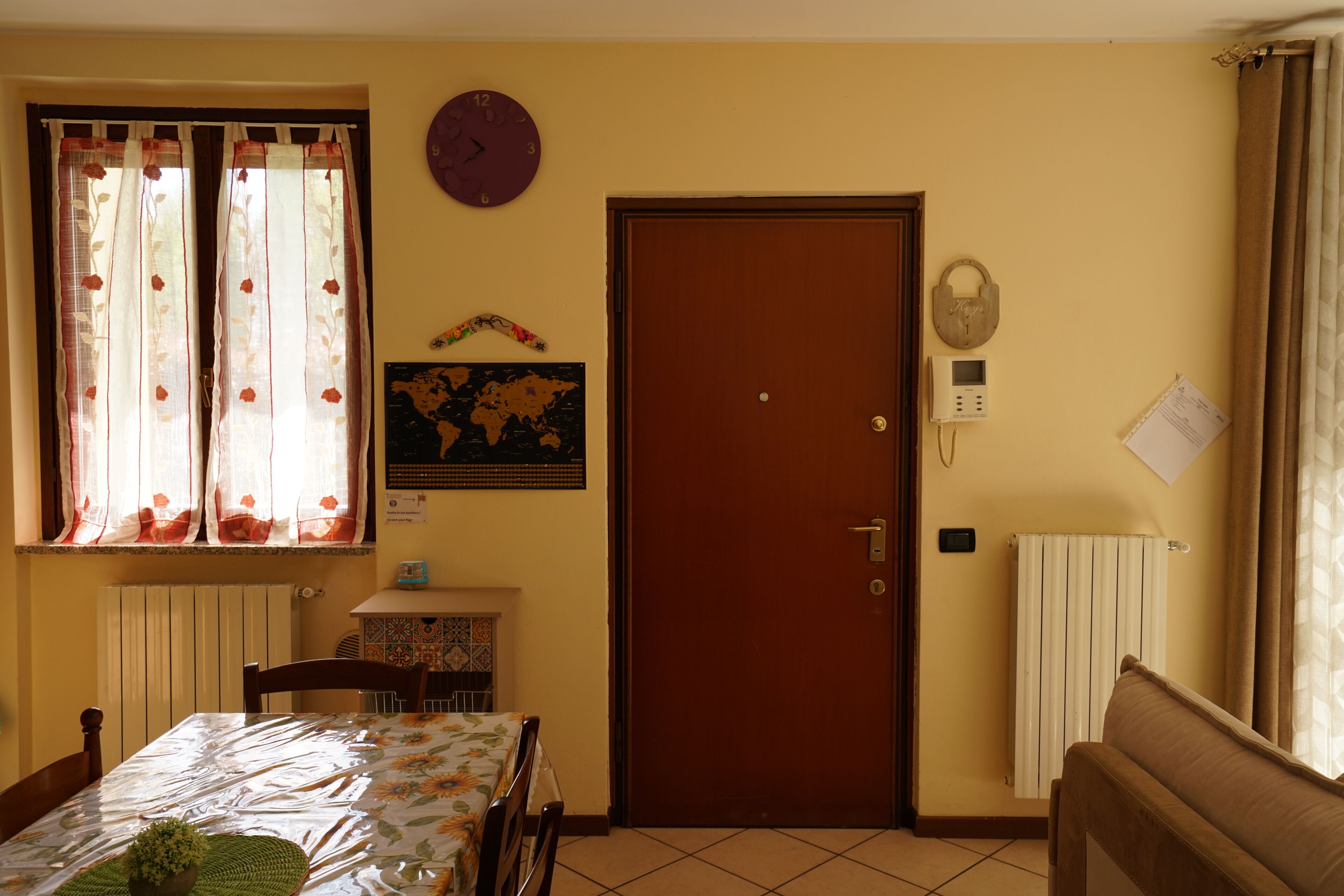 Ein Zimmer mit Holztür, einer Weltkarte an der Wand, einer Uhr und einem Heizkörper.