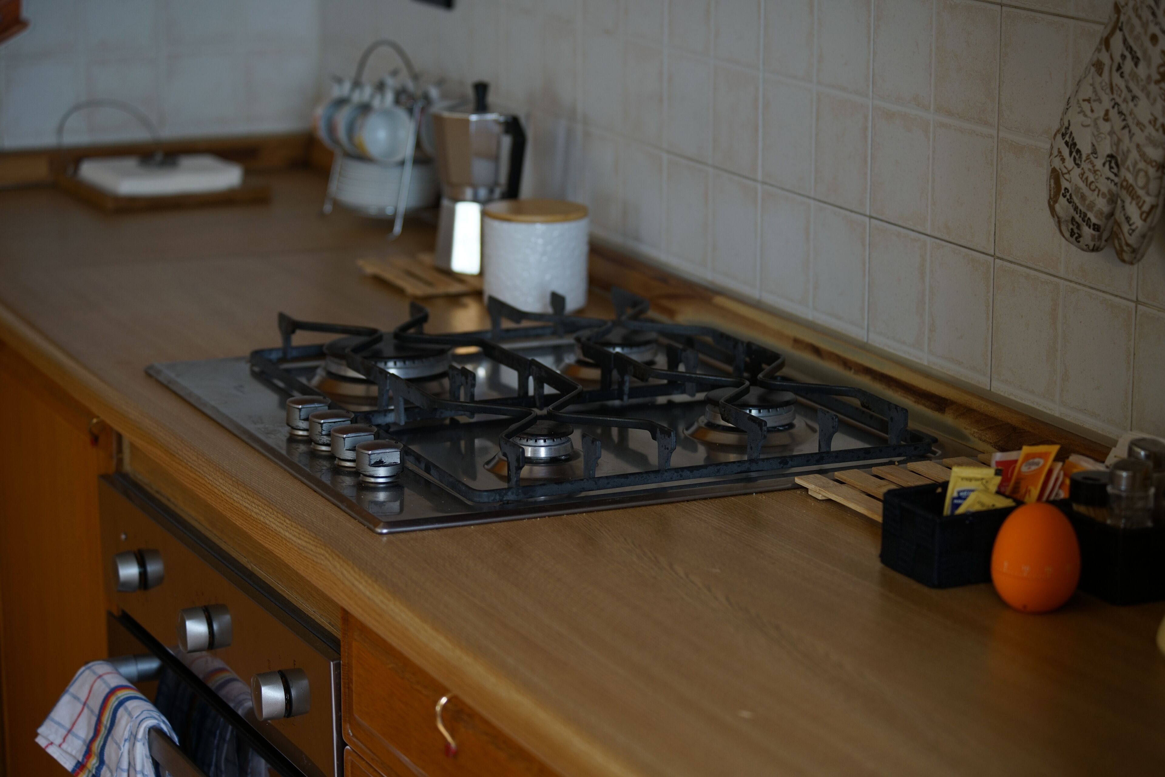 Cucina con piano cottura a gas, mobili in legno e un piano di lavoro con diversi oggetti.