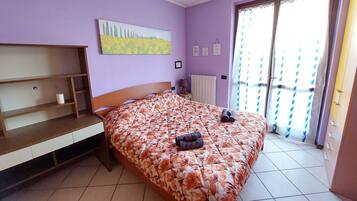 Une chambre à coucher avec un lit, une étagère en bois, un tableau, un radiateur et une fenêtre avec des rideaux.
