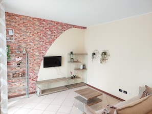 Ein Wohnzimmer mit Steinwand, Flachbildfernseher, Glastisch und einer Couch.