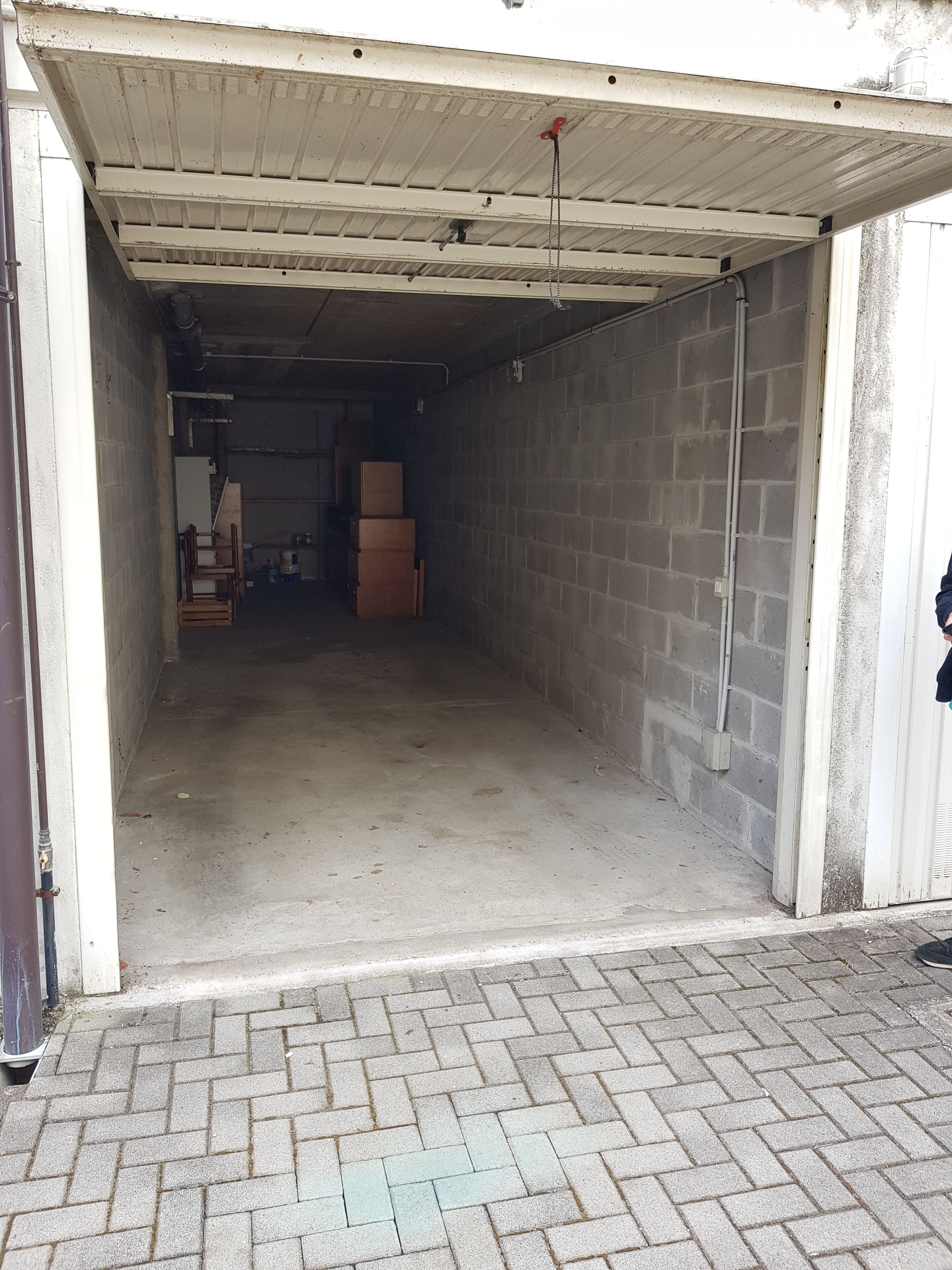 Ett garage med ett betonggolv, ett tak av metall och väggar av tegel. På vänster sida finns en trädörr och längst bak står en hög med kartonger.