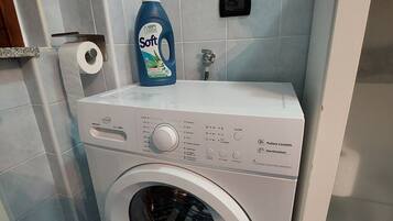 Een wasmachine met een voorlaadklep, een bedieningspaneel, een fles wasmiddel en een papieren handdoekdispenser.