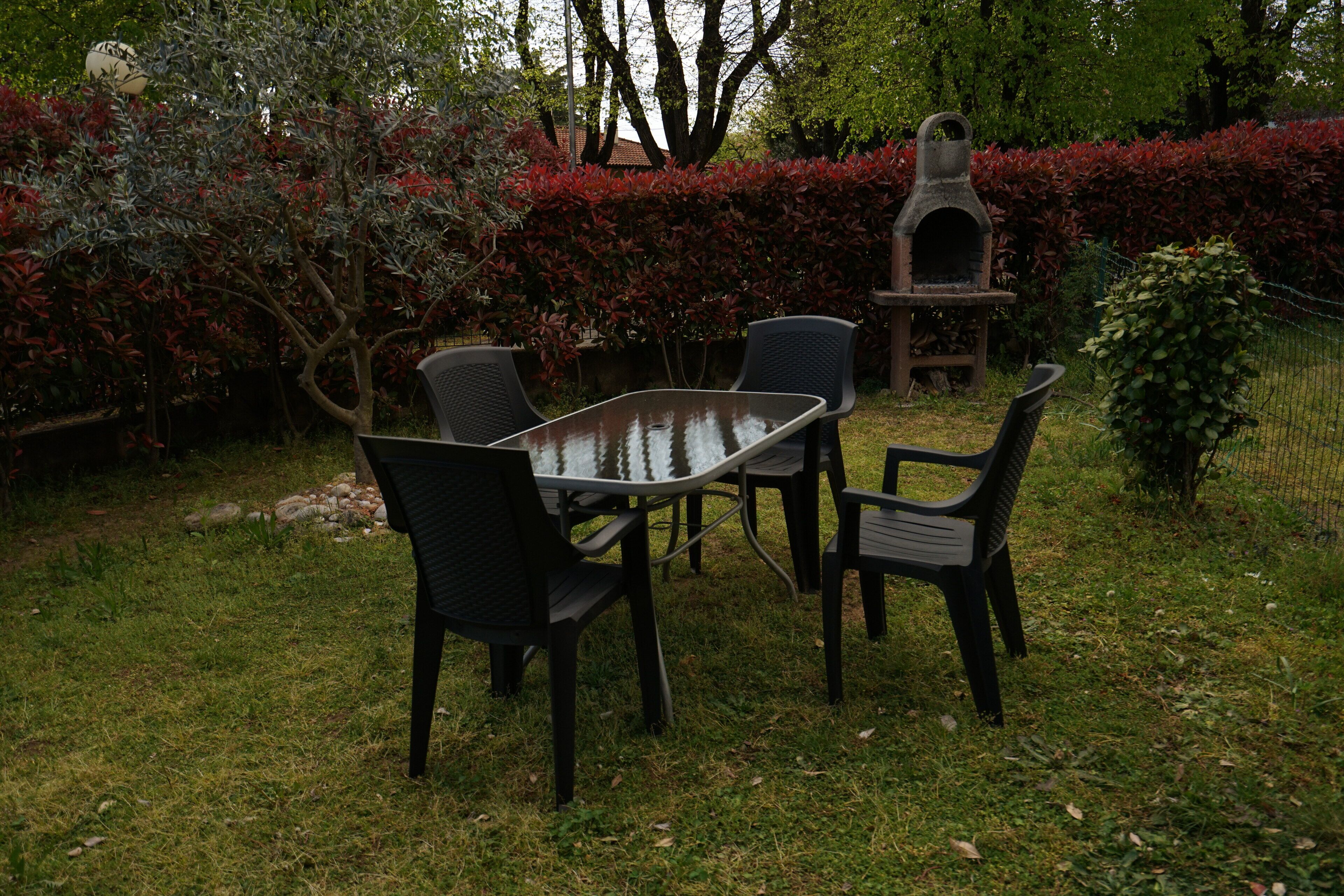 Patio esterno con tavolo e sedie, immerso nel verde e con un forno in pietra.