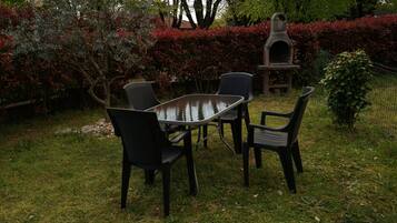 Patio esterno con tavolo e sedie, immerso nel verde e con un forno in pietra.