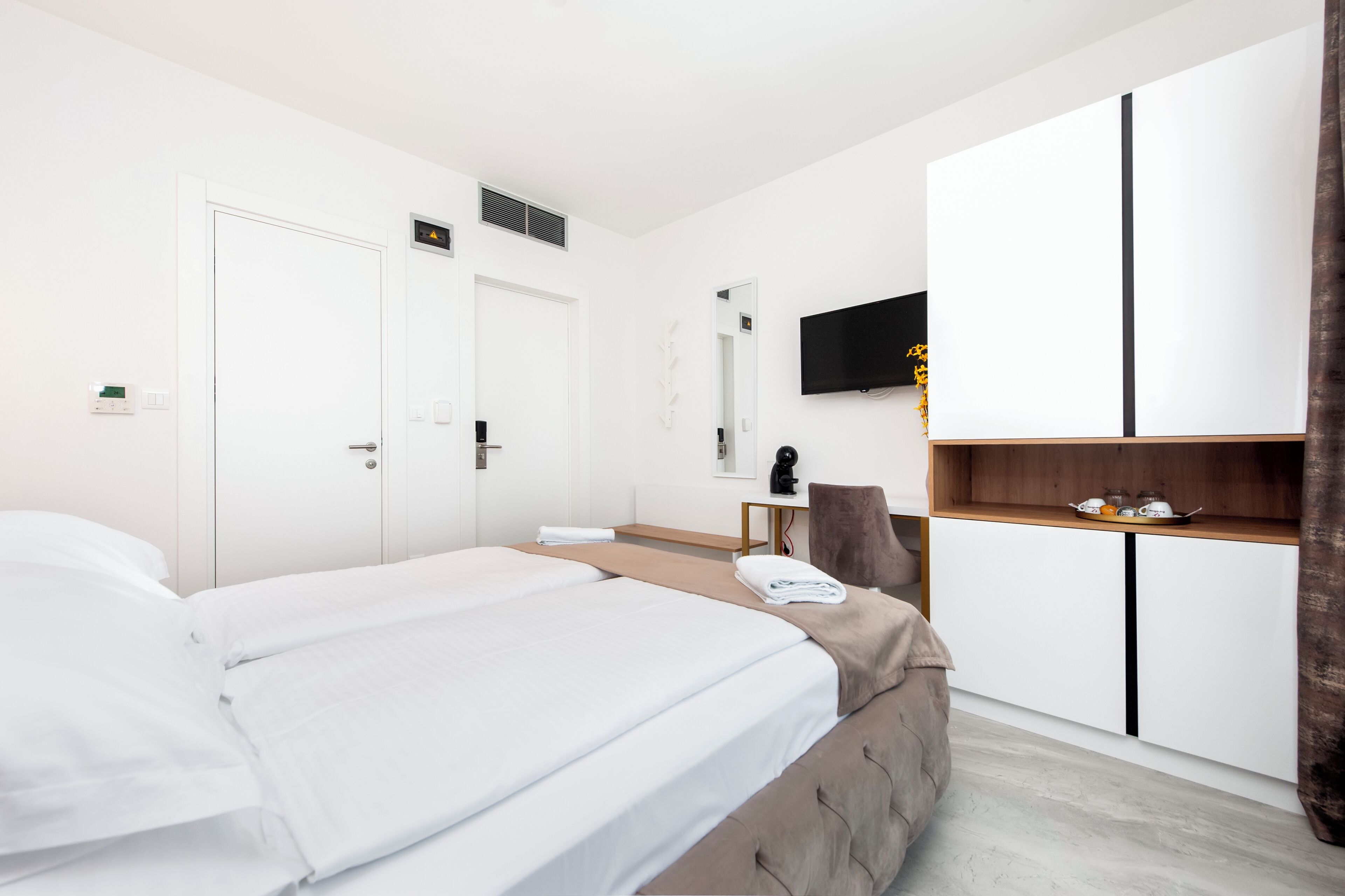 A modern hotel room with a large bed, a desk, a chair, a TV, and a wardrobe.