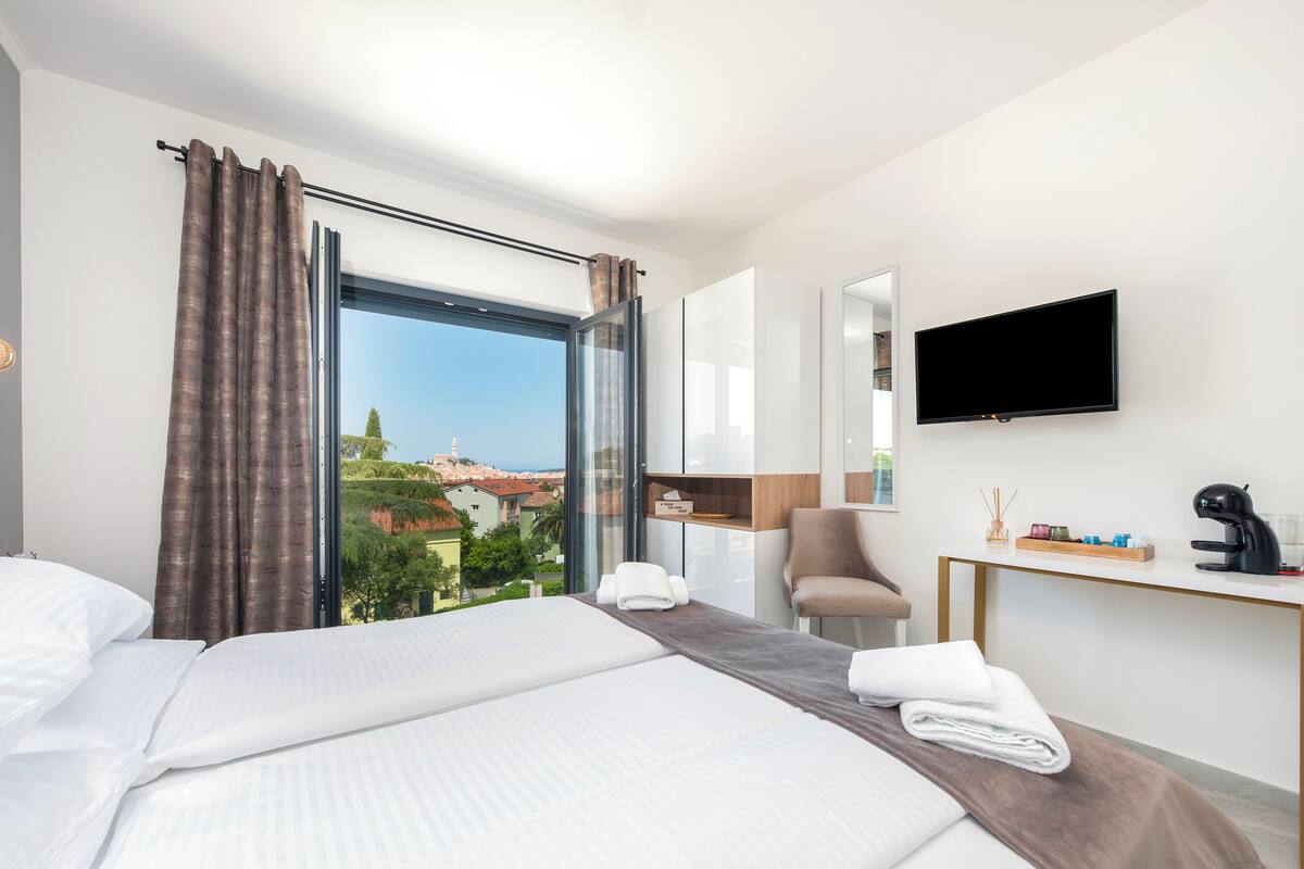 A modern hotel room with a large bed, a desk, a chair, and a TV.